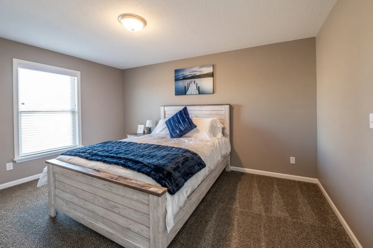 A cozy bed draped with a blue throw blanket and decorative pillows sits beneath calming wall art, forming an inviting nook ideal for reading or introspective moments. Soft natural light brightens the space, enhancing the sense of calm and personal renewal.