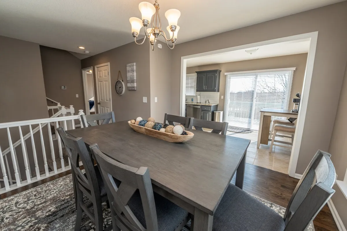 A welcoming dining area with an elegant table, chandelier, and decorative bowl, set adjacent to the kitchen entrance. The warm, inviting setup is ideal for shared meals, celebrations, or intimate conversations.