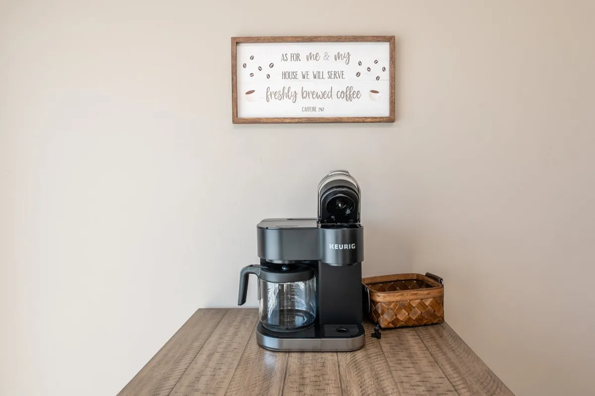 A cozy interior scene featuring a coffee maker, a decorative sign, and an inviting table surface, suggesting the pleasure of brewing and enjoying coffee at home. The atmosphere feels warm and welcoming, encouraging relaxation and connection before stepping outside.