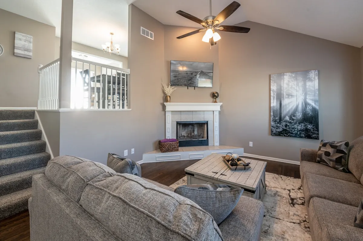 A cozy living room featuring a plush sofa set grouped around a fireplace and a central coffee table. Warm lighting and thoughtfully-placed wall art create an inviting atmosphere ideal for relaxation and social gatherings.
