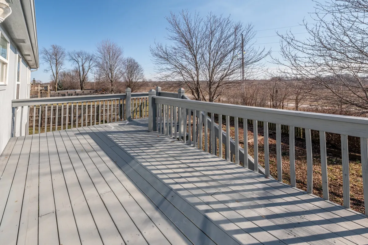 A close-up view of a wooden deck with sturdy railings, set against a backdrop of bare trees. The soft lighting suggests early morning or dusk, ideal for enjoying coffee at sunrise or a peaceful moment as the day winds down.